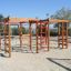 Kletteranlage aus Holz mit Klettergerüsten und Leiter auf Sandspielplatz.